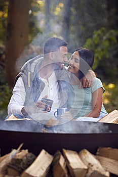 Romantic Couple Camping Sitting By Bonfire In Fire Bowl With Hot Drinks