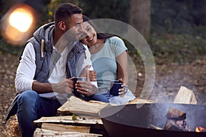 Romantic Couple Camping Sitting By Bonfire In Fire Bowl With Hot Drinks