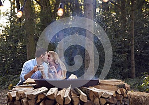 Romantic Couple Camping Sitting By Bonfire In Fire Bowl With Hot Drinks And Kissing