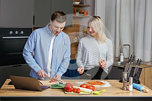 Romantic couple is cooking on kitchen. Handsome man and attractive young woman are having fun together while making salad and