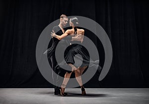 Romantic couple dance. Man and woman, professional tango dancers performing in black stage costumes over black