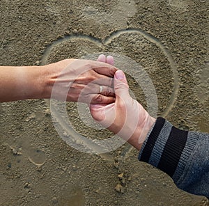 Romantic couple on date holding hands on heart sign background drawn on wet beach sand