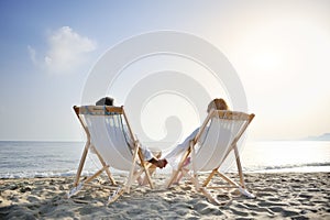 Romantic couple on deckchair relaxing enjoying sunset on the beach