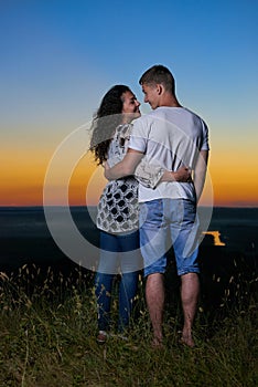 Romantic couple embrace at sunset, beautiful landscape and bright yellow sky, love tenderness concept, young adult people backside