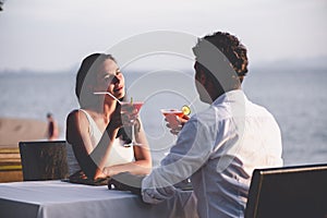 Romantic couple enjoy sunset in restaurant on the beach drinking cocktails