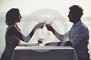 Romantic couple enjoy sunset in restaurant on the beach drinking cocktails