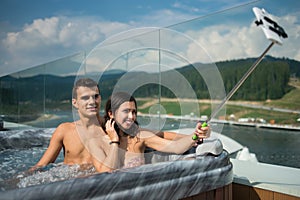 Romantic couple enjoying jacuzzi outdoors and making selfie photo on the phone with selfie stick