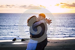 Romantic couple enjoying sunset at the beach kissing and loving each other - caucasian people have romance summer time holiday