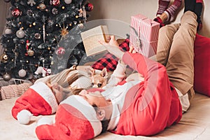 Romantic couple exchanging gifts near decorated christmas tree. Man giving christmas present surprise to smiling woman in sweater