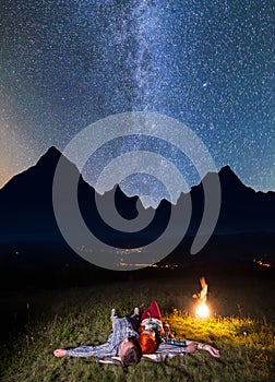 Romantic couple - girl and guy lying near the fire, enjoying incredibly beautiful starry sky. Long exposure