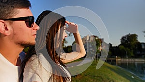 Romantic couple in a green summer park near the pond. Young smiling couple talking, hugging at sunny park, candy-flower