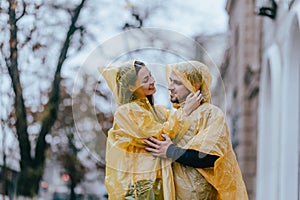 Romantic couple, guy and his girlfriend dressed in yellow raincoats are hugging on the street in the rain