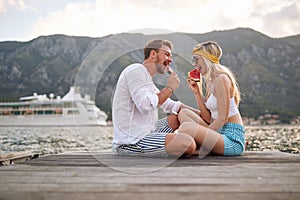 Romantic couple having date on pier by water eating watermelon. Fun, love, togetherness, lifestyle concept