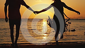 Romantic couple holding hands running to the beach on amazing sunset. Having fun together at vacation. Slow motion