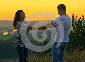 Romantic couple holding hands at sunset on outdoor, beautiful landscape and bright yellow sky, love tenderness concept, young