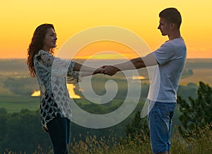 Romantic couple holding hands at sunset on outdoor, beautiful landscape and bright yellow sky, love tenderness concept, young