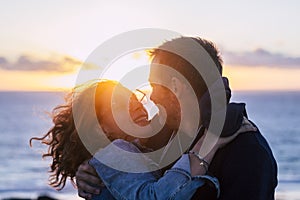 Romantic couple hug and kiss having fun and laughing a lot with beautiful sunset and ocean in background - concept of adults in