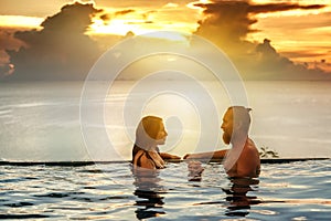 Romantic couple in the infinity pool at sunset overlooking the s