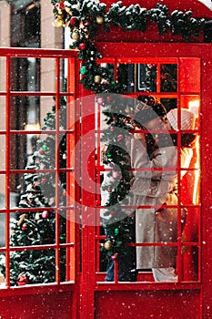 Romantic couple kissing, hugging, having fun in winter before Christmas, standing in red phone booth