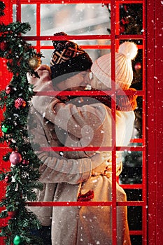 Romantic couple kissing, hugging, having fun in winter before Christmas, standing in red phone booth