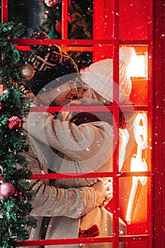 Romantic couple kissing, hugging, having fun in winter before Christmas, standing in red phone booth