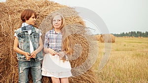 Romantic couple leaning back on haystack on harvesting field in countryside. Teenager girl and boy standing on haystack
