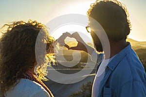 Romantic couple in love doing heart symbol with hands against an amazing golden sunset. Man and woman flirting and dating outdoor