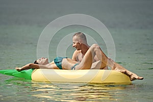 Romantic couple lying on bed. Man and woman on honeymoon, swim on pineapple shaped mattress in sea. Happy young couple