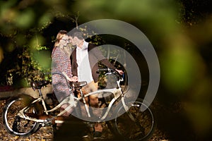 Romantic couple, man and attractive girl close together at tandem bicycle in dark autumn park.