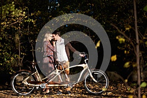 Romantic couple, man and attractive girl close together at tandem bicycle in dark autumn park.