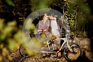 Romantic couple, man and attractive girl close together at tandem bicycle in dark autumn park.
