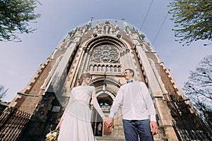 Romantic couple, newlywed valentynes posing holding hands near old gothic church