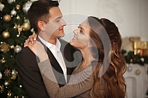 Romantic couple portrait in love. Cheerful Happy newlywed hugging by xmas tree in Christmas interior on winter holidays.