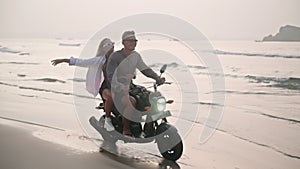 Romantic couple ride motorbike on ocean beach on a date at sunrise. Lovers travel by motorcycle on coastline along water