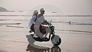 Romantic couple ride motorbike on ocean beach on a date at sunrise. Lovers travel by motorcycle on coastline along water