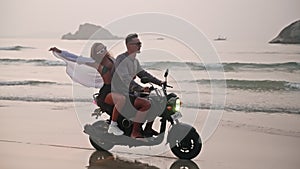 Romantic couple ride motorbike on ocean beach on at sunrise in slomo. Lovers travel by motorcycle on coastline along