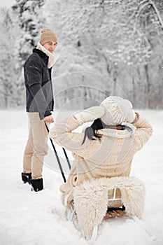 Romantic couple riding on a sled in forest at winter day