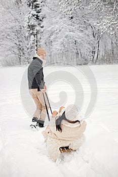 Romantic couple riding on a sled in forest at winter day