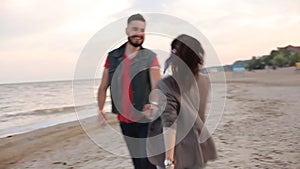 Romantic couple running holding hands on white sand beach near sea in slow motion. Boyfriend and girlfriend having fun