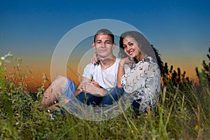 Romantic couple sit on grass at sunset on outdoor, beautiful landscape and dark night sky sky, love tenderness concept, young