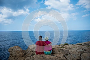 Romantic couple sitting on a cliff and admirig wonderful seascape