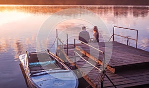 Romantic couple sitting pier golden sunset. Beautiful nature lake. man woman meet sunset. Beautiful couple outdoors near water