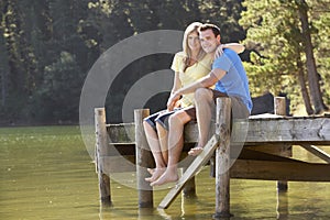 Romantic Couple Sitting On Wooden Jetty Looking Out Over Lake
