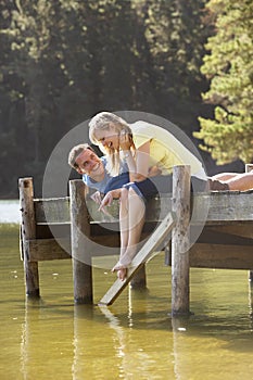 Romantic Couple Sitting On Wooden Jetty Looking Out Over Lake