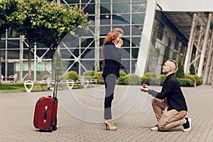 Romantic couple standing near the airport with a suitcase. Man makes an offer to his attractive young woman