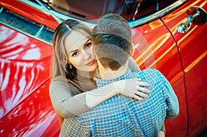 A romantic couple is standing by the red car. A man is hugging a woman. American classics. The guy and the girl next to the red ca