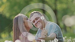 Romantic couple in summer on a clearing among white dandelions. They joyfully blow and spray dandelions. Happy together