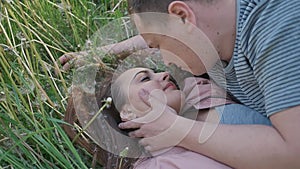 Romantic couple in summer on a glade. The girl lies in the grass among white dandelions. The guy touches the girl`s hair