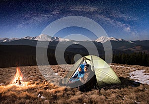 Romantic couple tourists having a rest in the camping at night under beautiful night sky full of stars and milky way