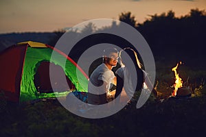 Romantic couple of tourists near the fire sit at to the camping.